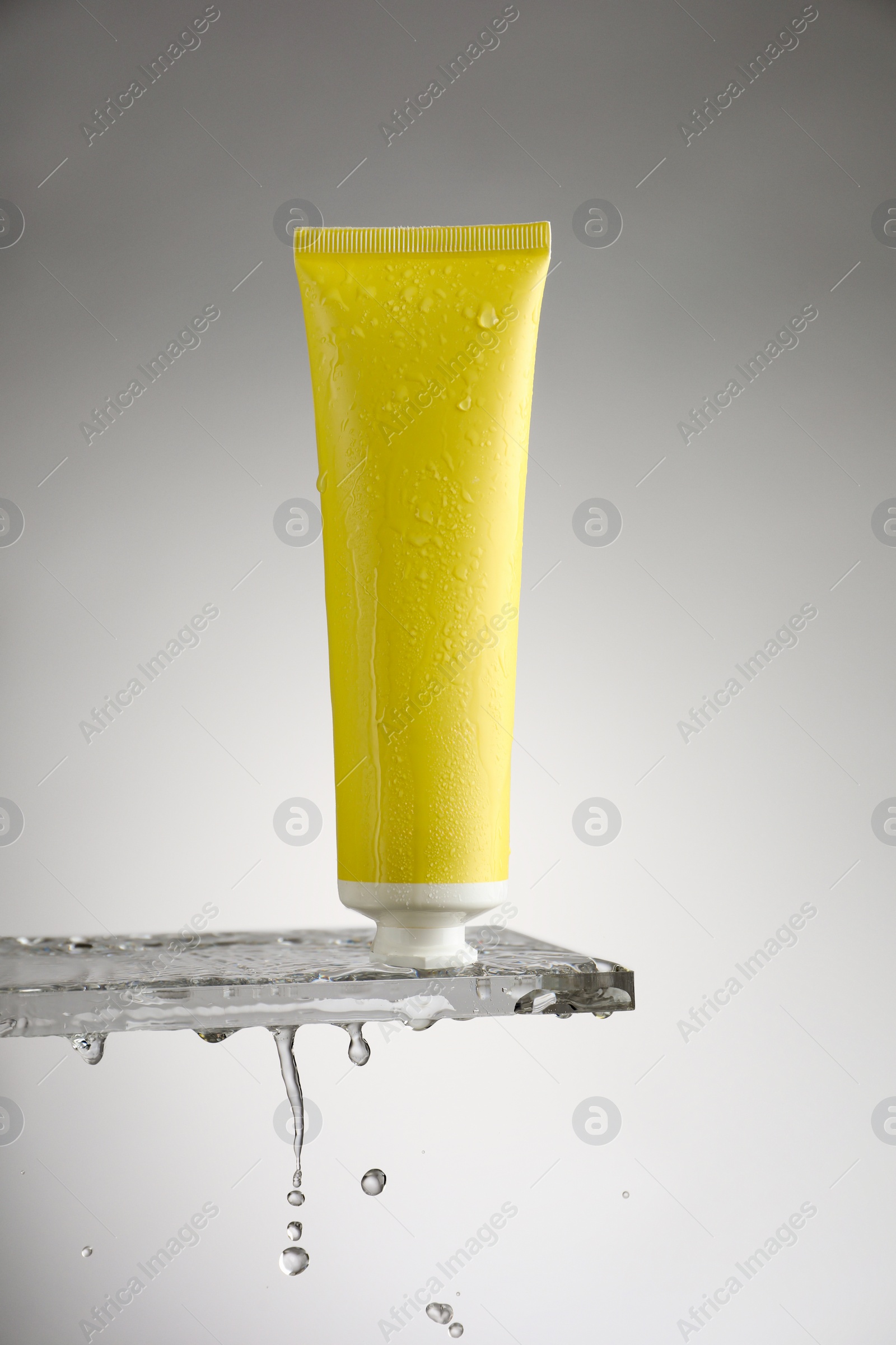 Photo of Moisturizing cream in tube on glass with water drops against grey background