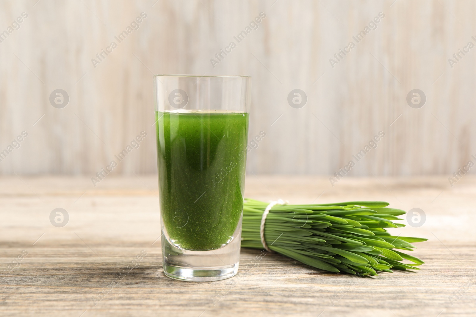 Photo of Wheat grass drink in shot glass and fresh green sprouts on wooden table, closeup