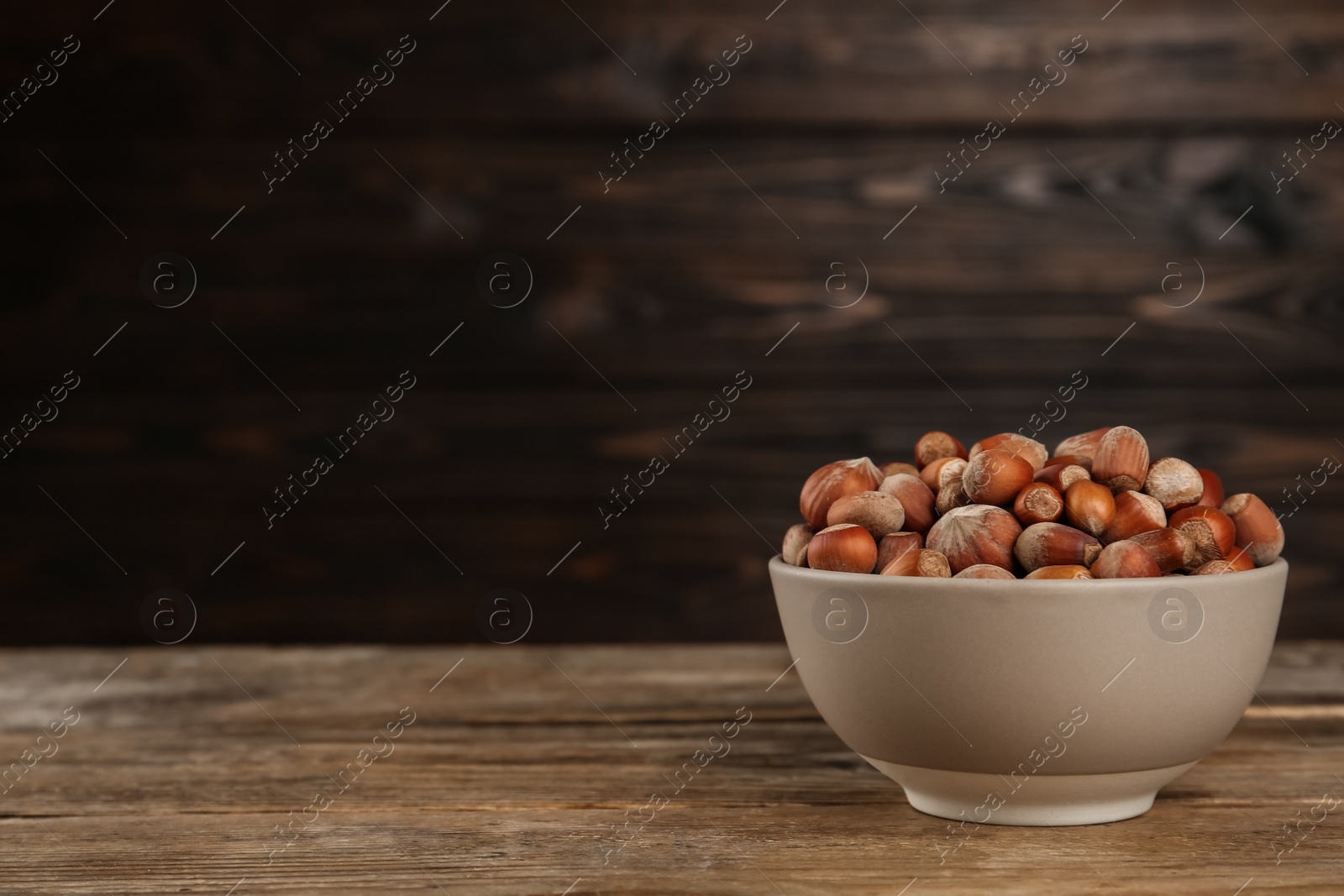 Photo of Ceramic bowl with acorns on wooden table, space for text. Cooking utensil