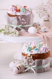 Photo of Traditional Easter cakes with meringues and painted eggs on white wooden table