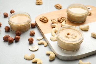 Different types of delicious nut butters and ingredients on light table, closeup