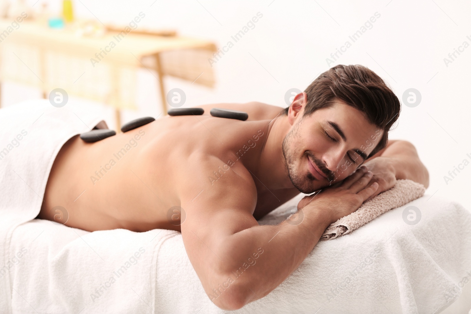 Photo of Handsome young man receiving hot stone massage in spa salon