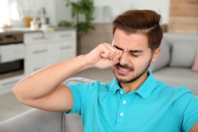 Young man rubbing eye at home. Annoying itch