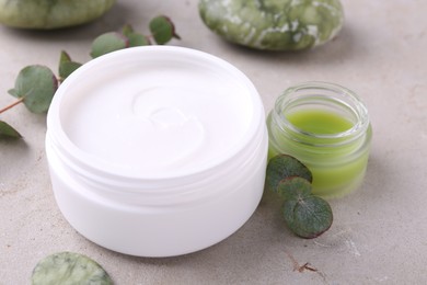 Photo of Jars of cream and green leaves on light textured table. Body care products