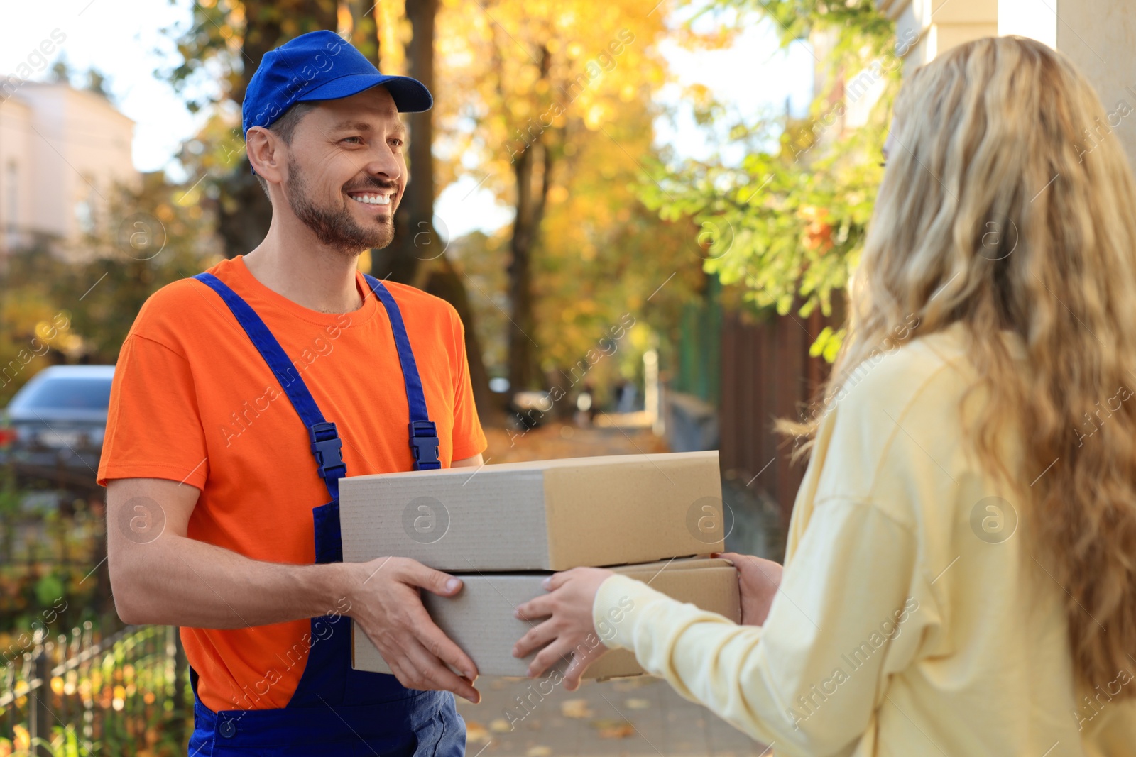 Photo of Woman receiving parcels from courier in uniform outdoors