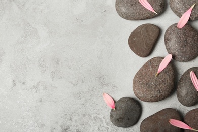 Spa stones with flower petals and space for text on grey background, flat lay