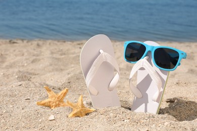 Photo of Stylish flip flops, sunglasses and starfishes on sandy beach