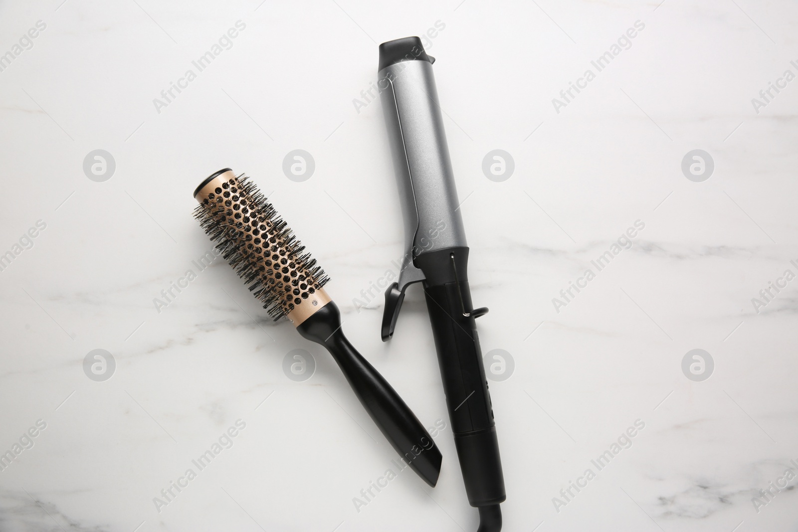 Photo of Curling iron and round hair brush on white marble background, flat lay