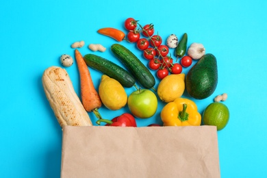 Photo of Paper bag with different groceries on light blue background, flat lay