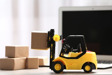 Photo of Toy forklift with box near laptop on table. Logistics and wholesale concept