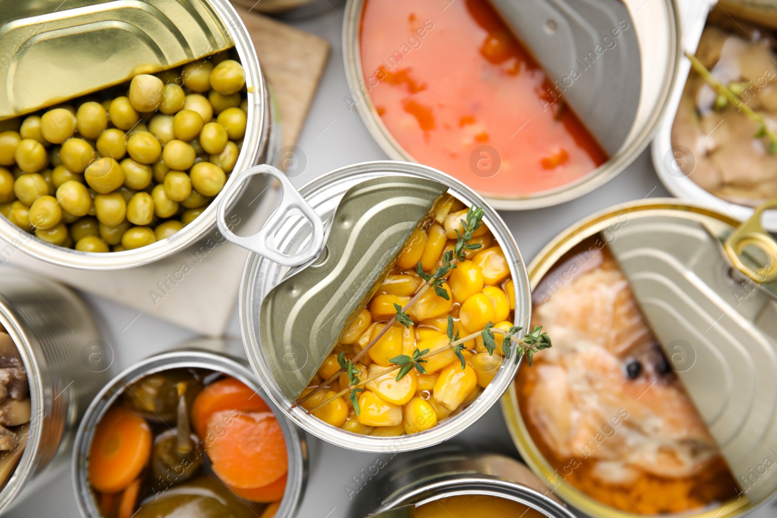 Photo of Open tin cans with different products on table, flat lay