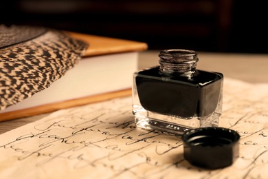 Open inkwell, feather, book and vintage parchment with text on table, closeup