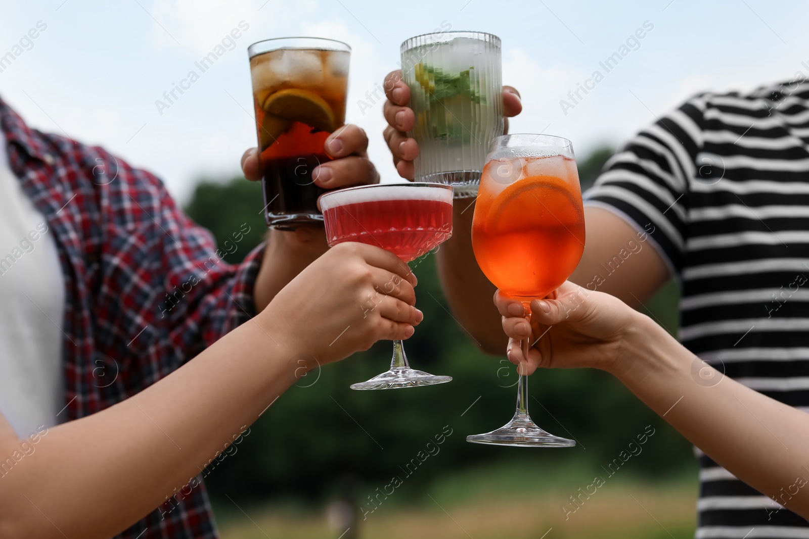 Photo of Friends clinking glasses with cocktails outdoors, closeup