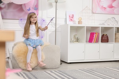 Photo of Cute little girl in fairy costume with violet wings and magic wand at home, space for text