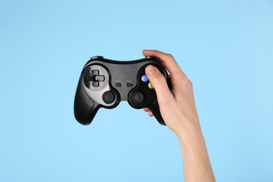 Woman with game controller on light blue background, closeup