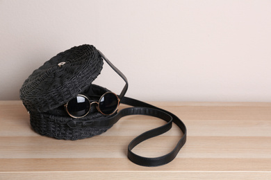 Stylish woman's bag and sunglasses on wooden table. Space for text