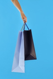 Woman with paper shopping bags on light blue background, closeup