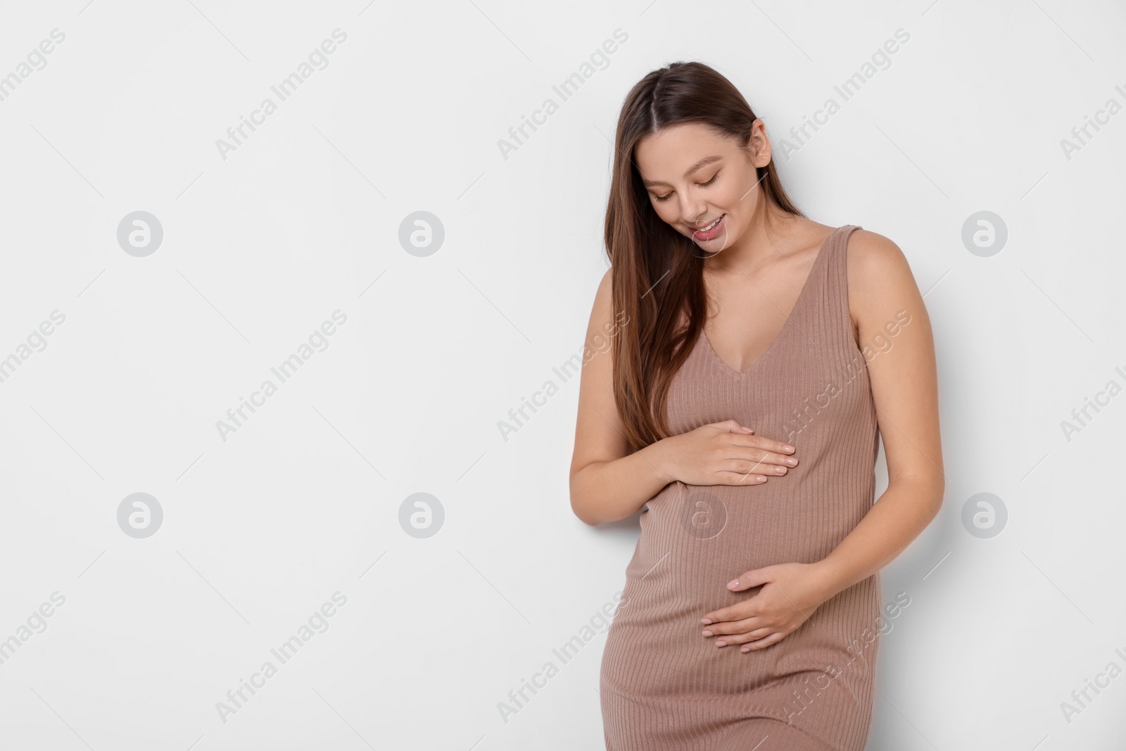 Photo of Beautiful pregnant woman in beige dress on white background, space for text