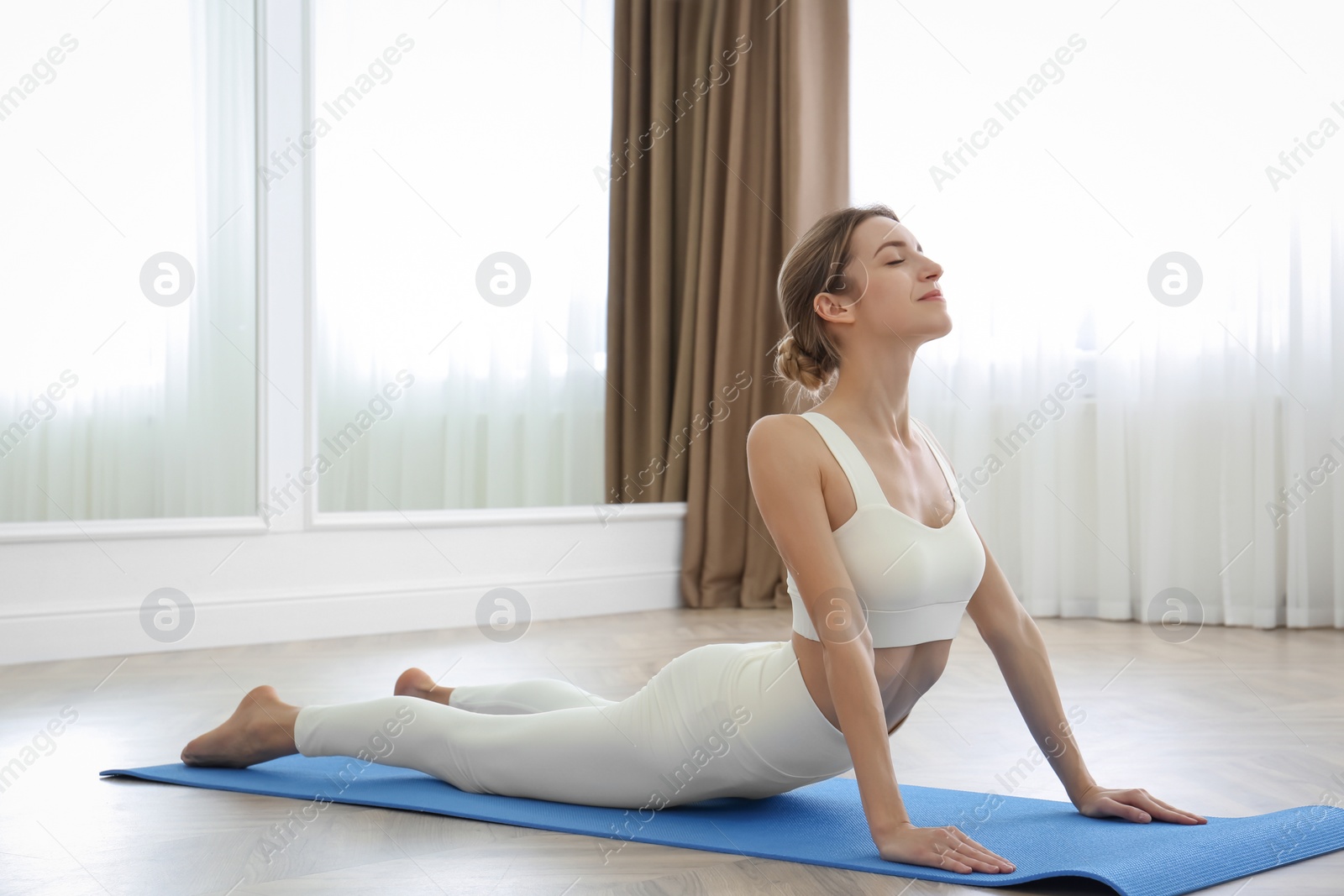 Photo of Young woman practicing high cobra asana in yoga studio. Bhujangasana pose