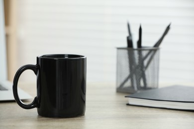 Black ceramic mug on wooden table indoors. Space for text