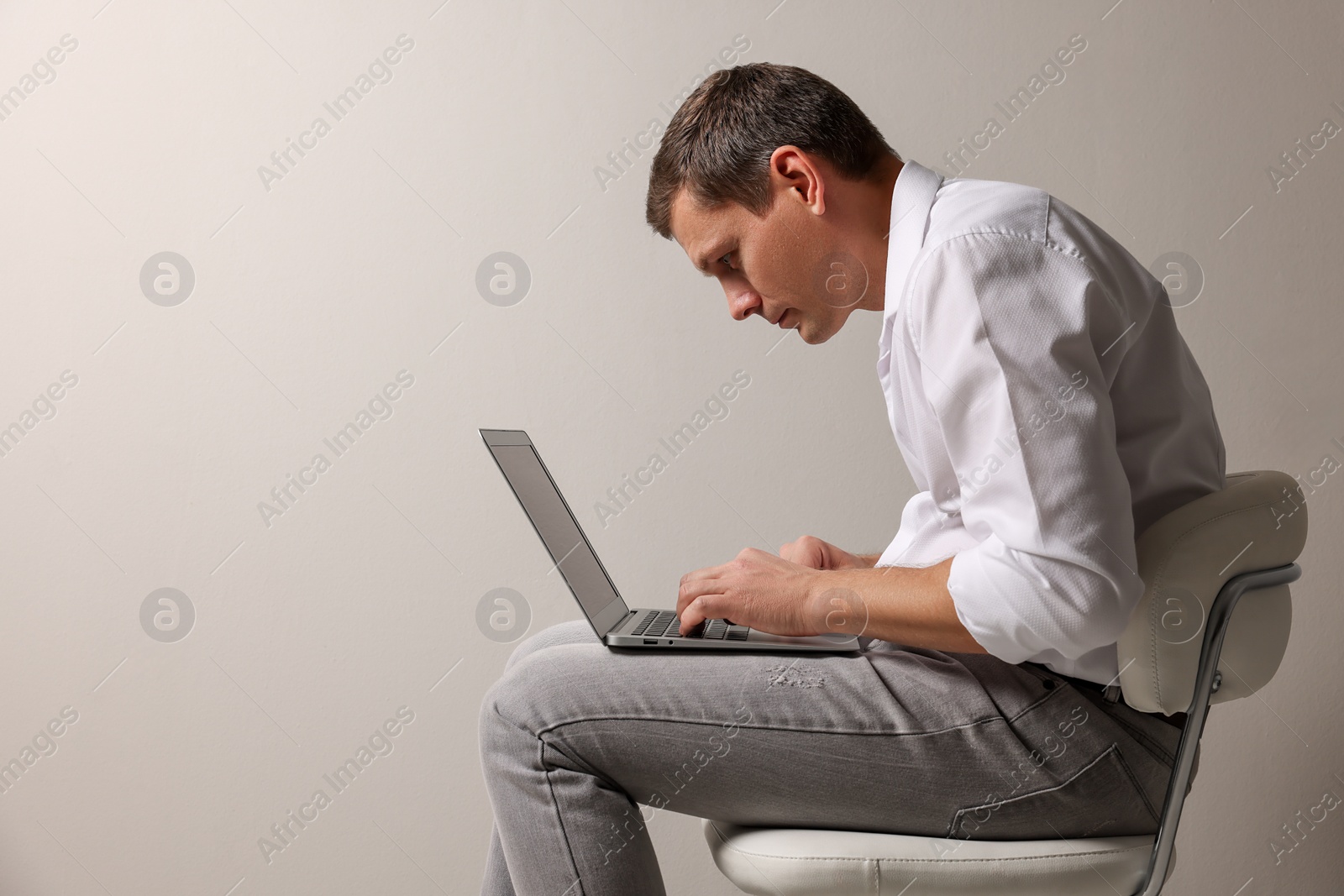 Photo of Man with bad posture using laptop while sitting on chair against grey background. Space for text