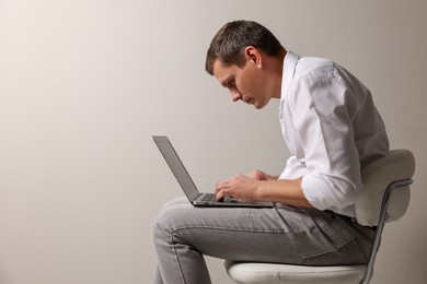 Photo of Man with bad posture using laptop while sitting on chair against grey background. Space for text