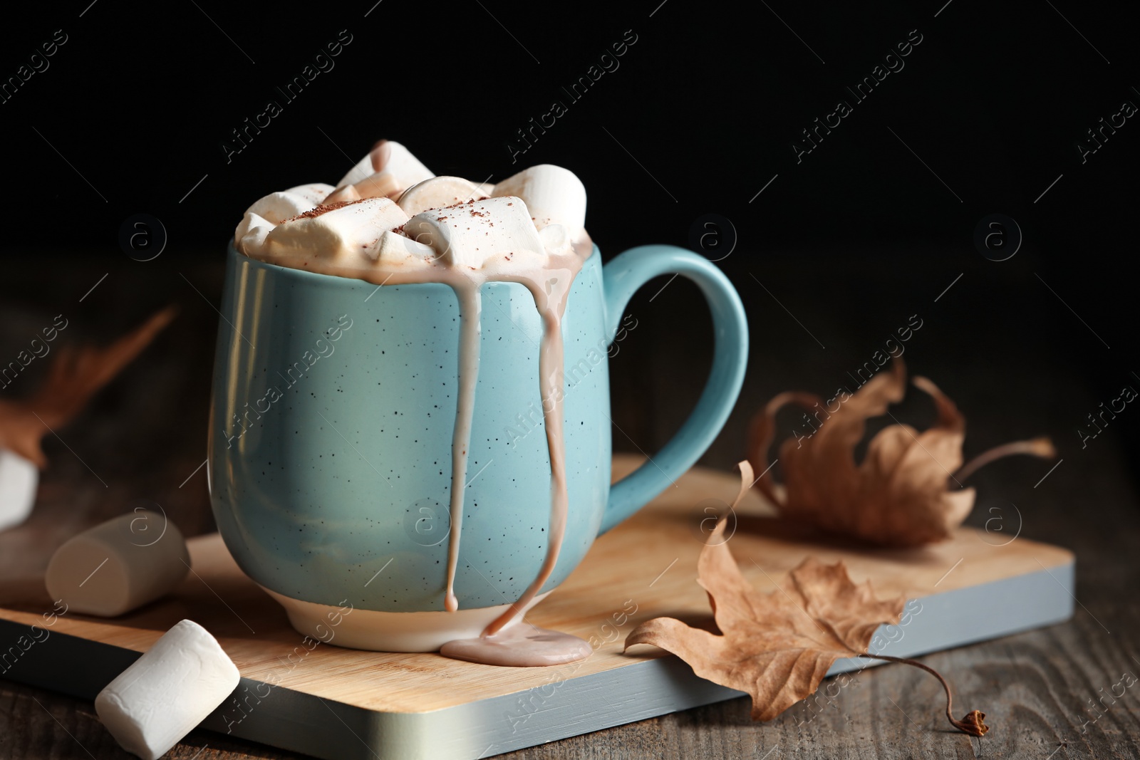 Photo of Pouring hot cozy drink into cup near autumn leaves on table. Space for text