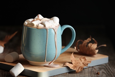 Pouring hot cozy drink into cup near autumn leaves on table. Space for text