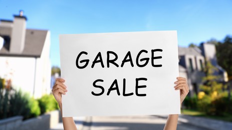 Image of Woman holding sign with text GARAGE SALE on street, closeup