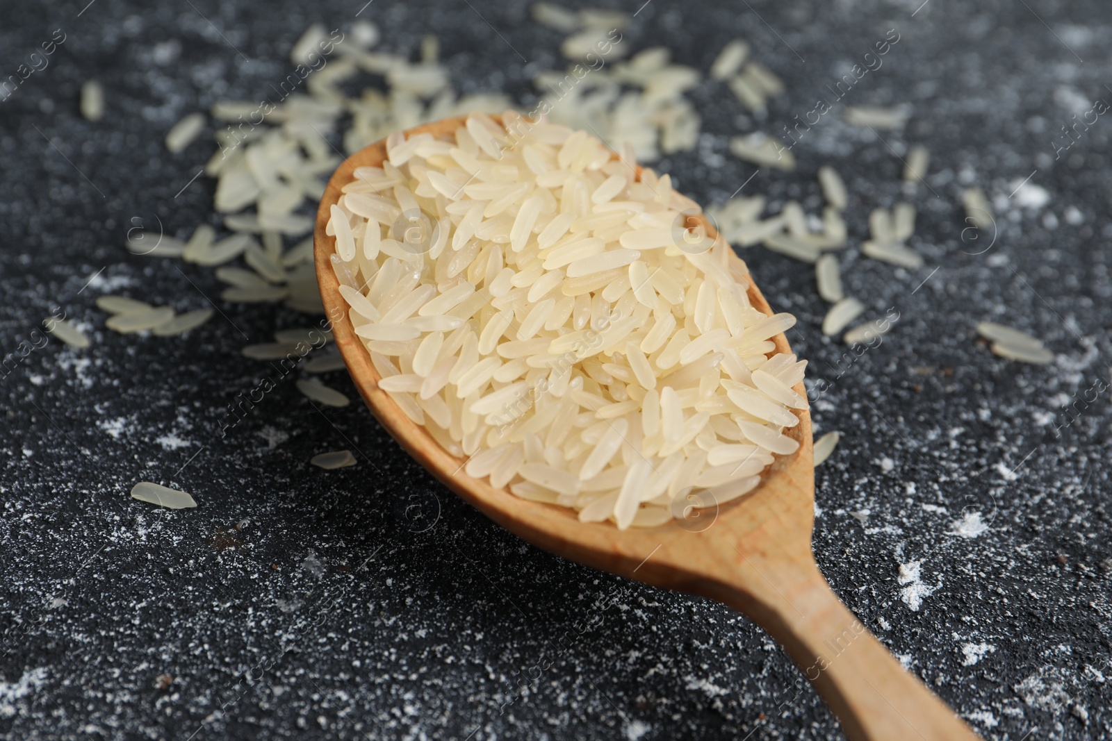 Photo of Spoon with raw rice on black textured table, closeup