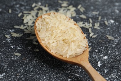 Photo of Spoon with raw rice on black textured table, closeup