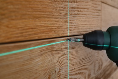 Using cross line laser level for accurate measurement and driving screw in wooden wall, closeup