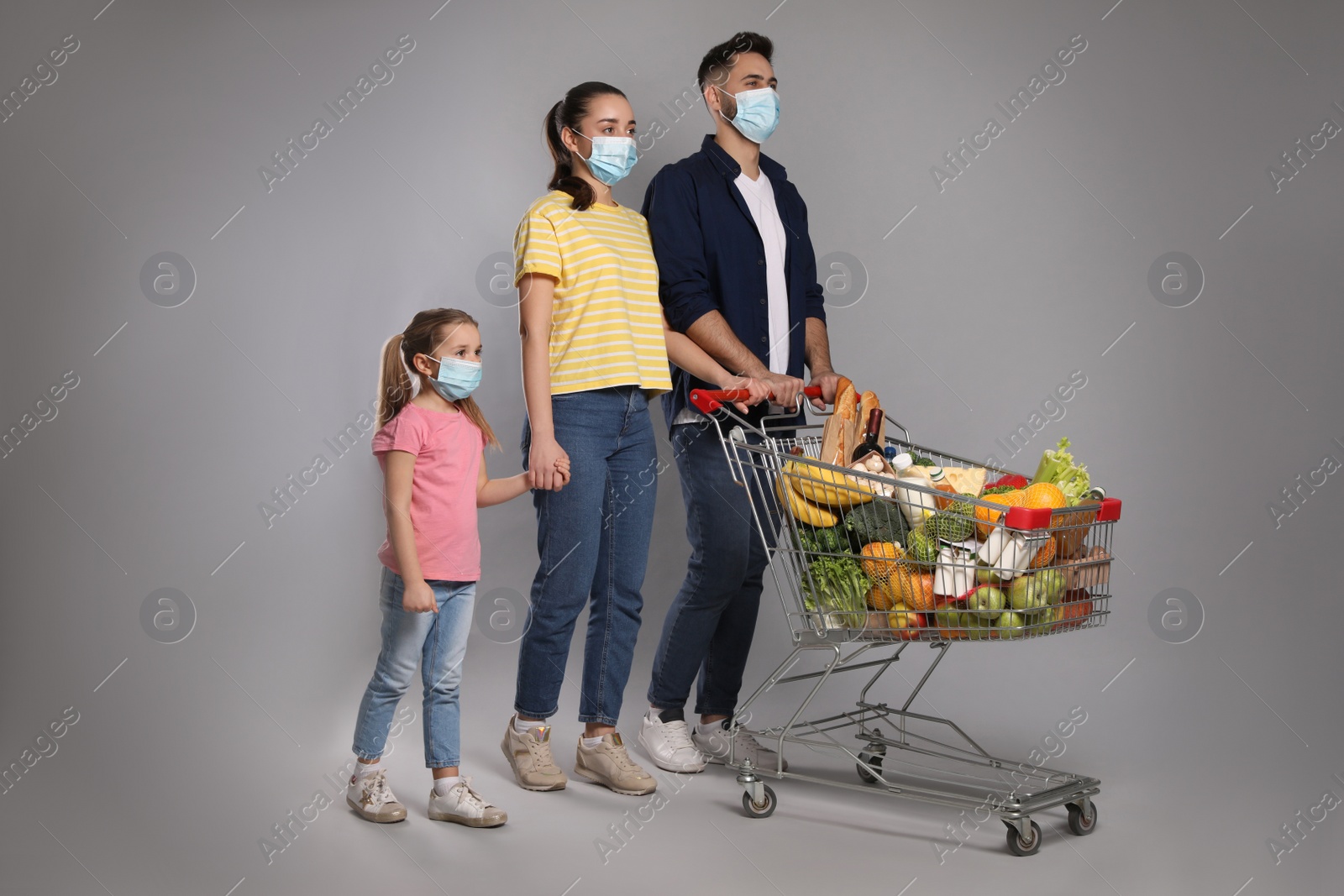 Photo of Family with protective masks and shopping cart full of groceries on light grey background