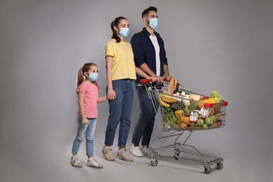 Photo of Family with protective masks and shopping cart full of groceries on light grey background