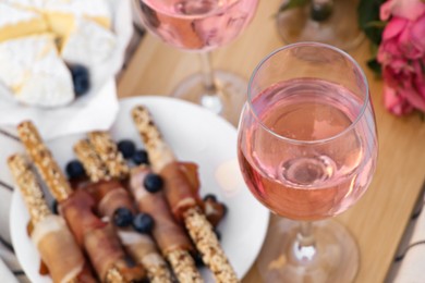 Photo of Glasses of delicious rose wine, flowers and food on wooden board, closeup