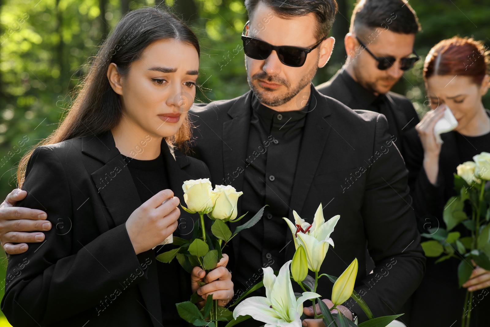 Photo of Sad people with flowers mourning outdoors. Funeral ceremony