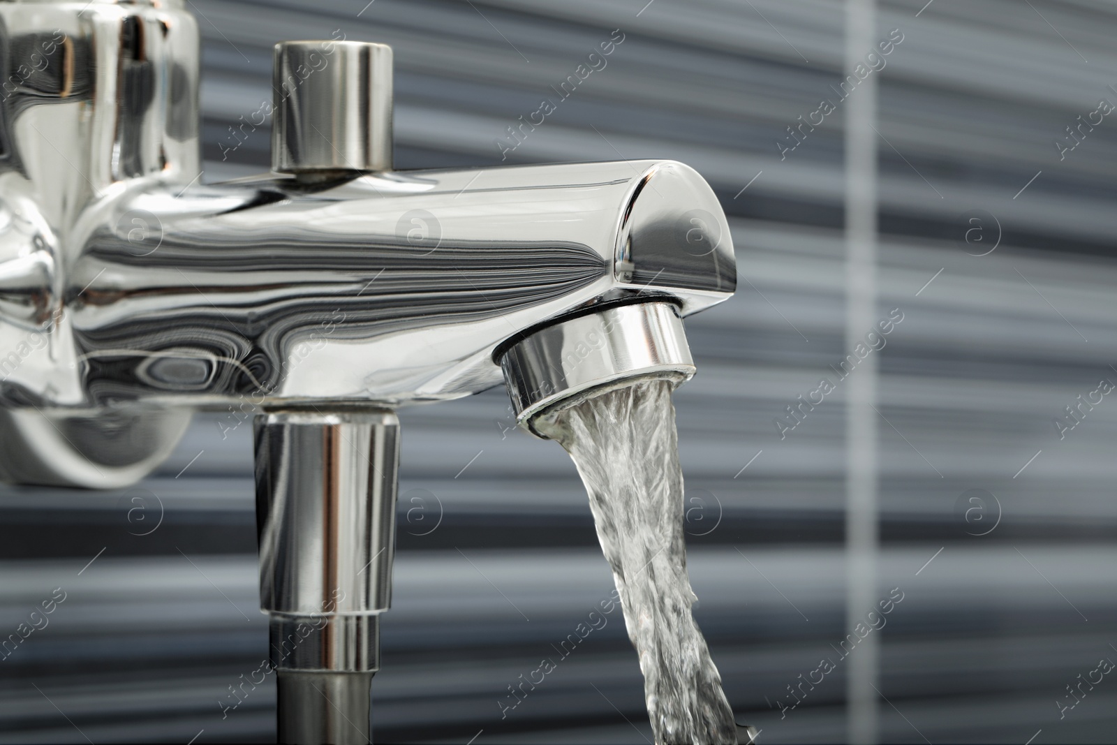 Photo of Water flowing from bath tap on blurred background, closeup