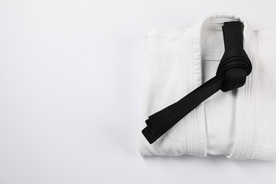 Black karate belt and kimono on white background, top view. Space for text