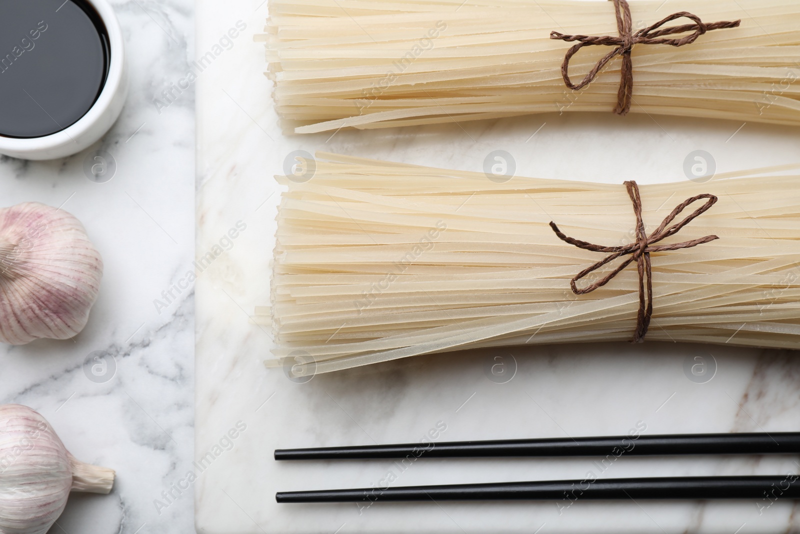 Photo of Flat lay composition with uncooked rice noodles, soy sauce and chopsticks on white marble table