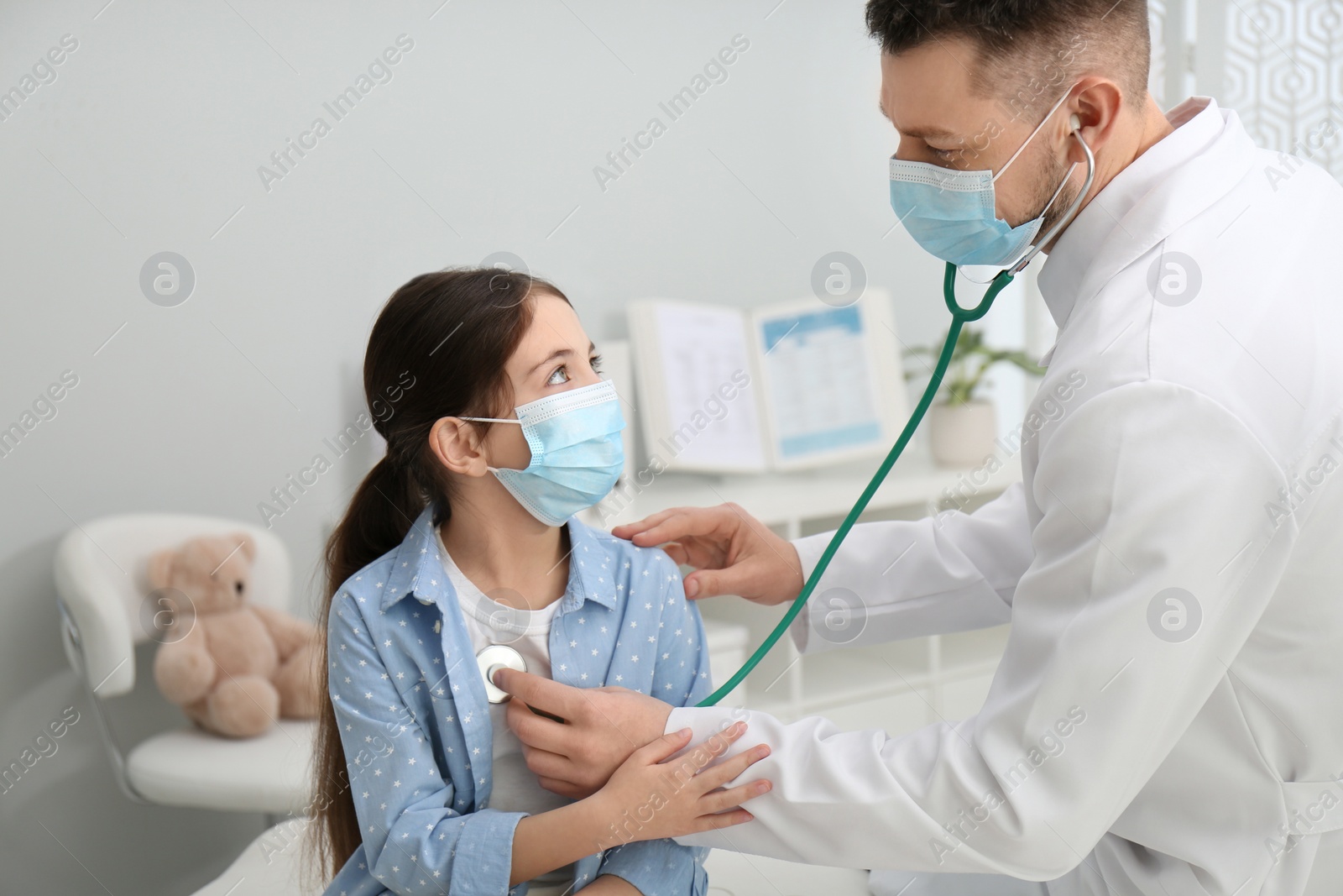 Photo of Pediatrician examining little girl in hospital. Doctor and patient wearing protective masks