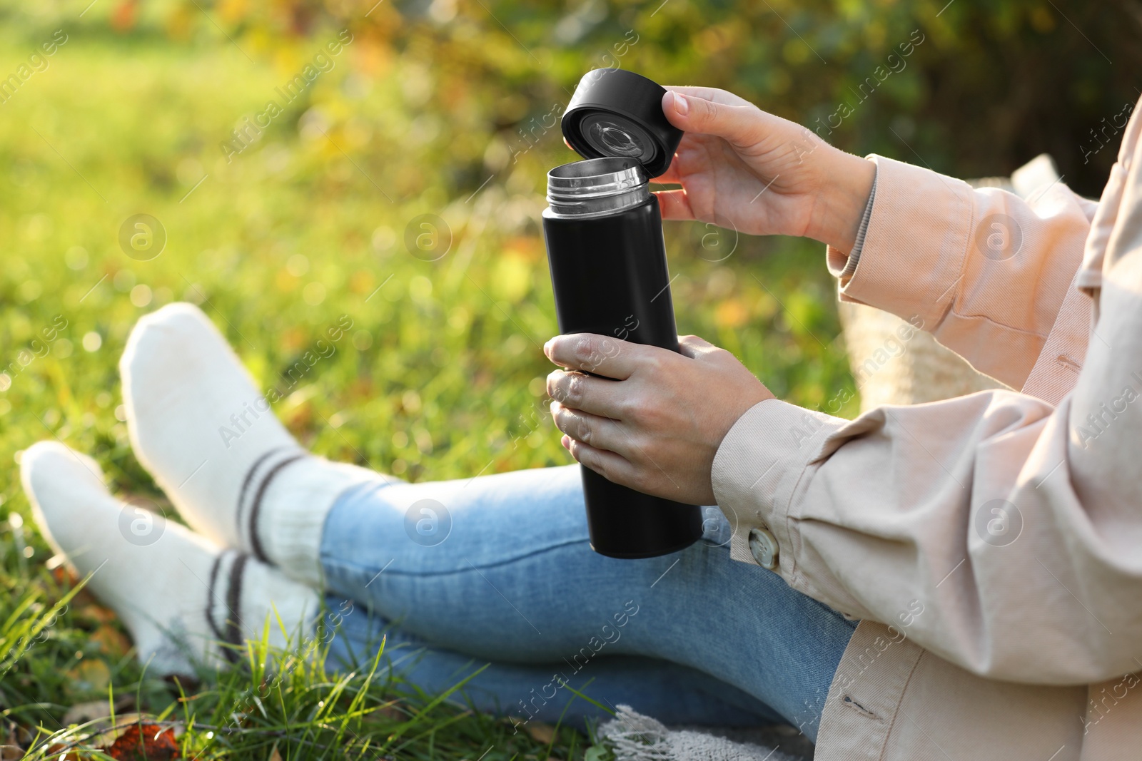 Photo of Woman opening thermos on green grass outdoors, closeup