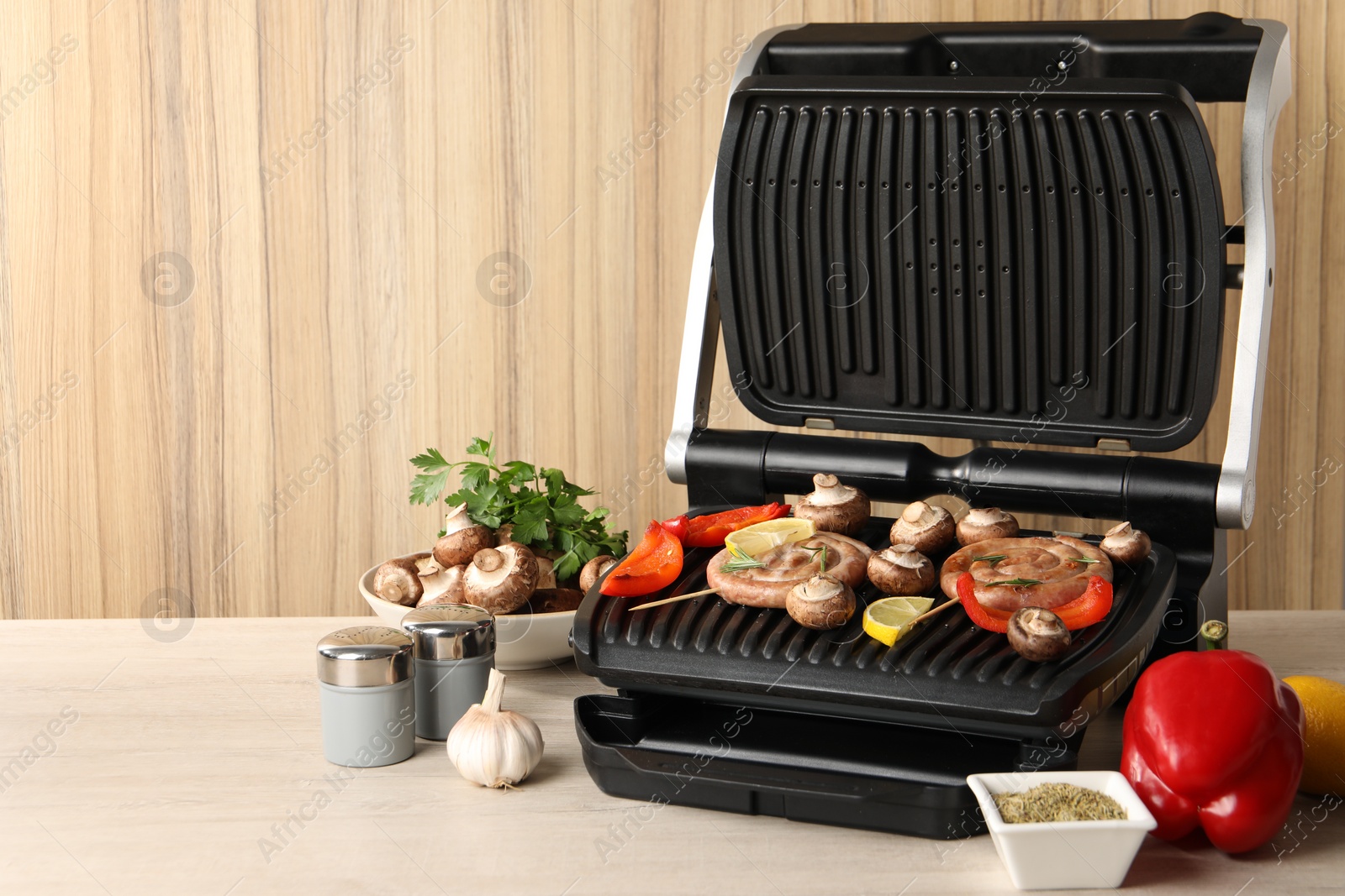 Photo of Electric grill with homemade sausages, vegetables and spices on wooden table