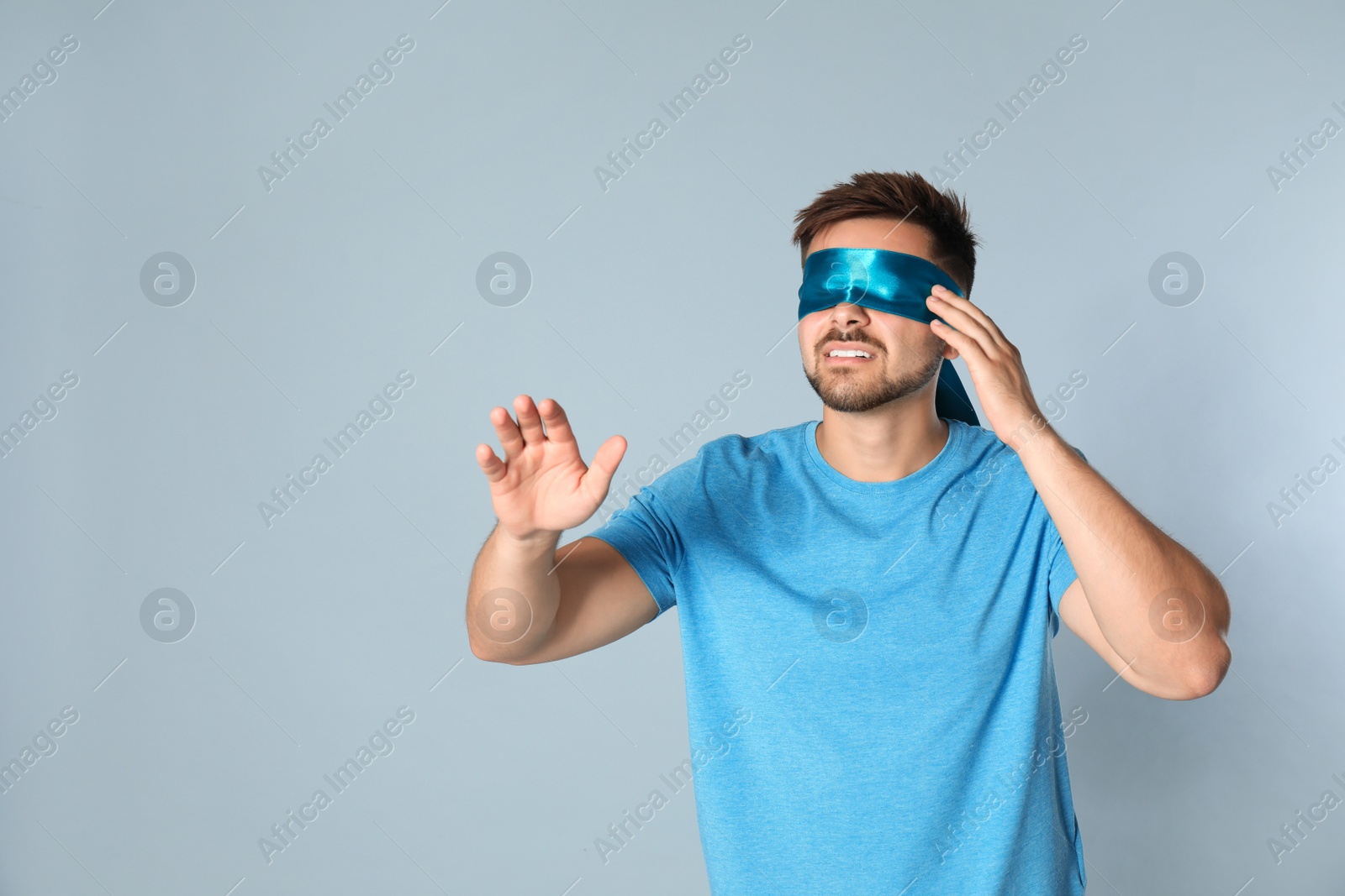 Photo of Young man with light blue blindfold on grey background