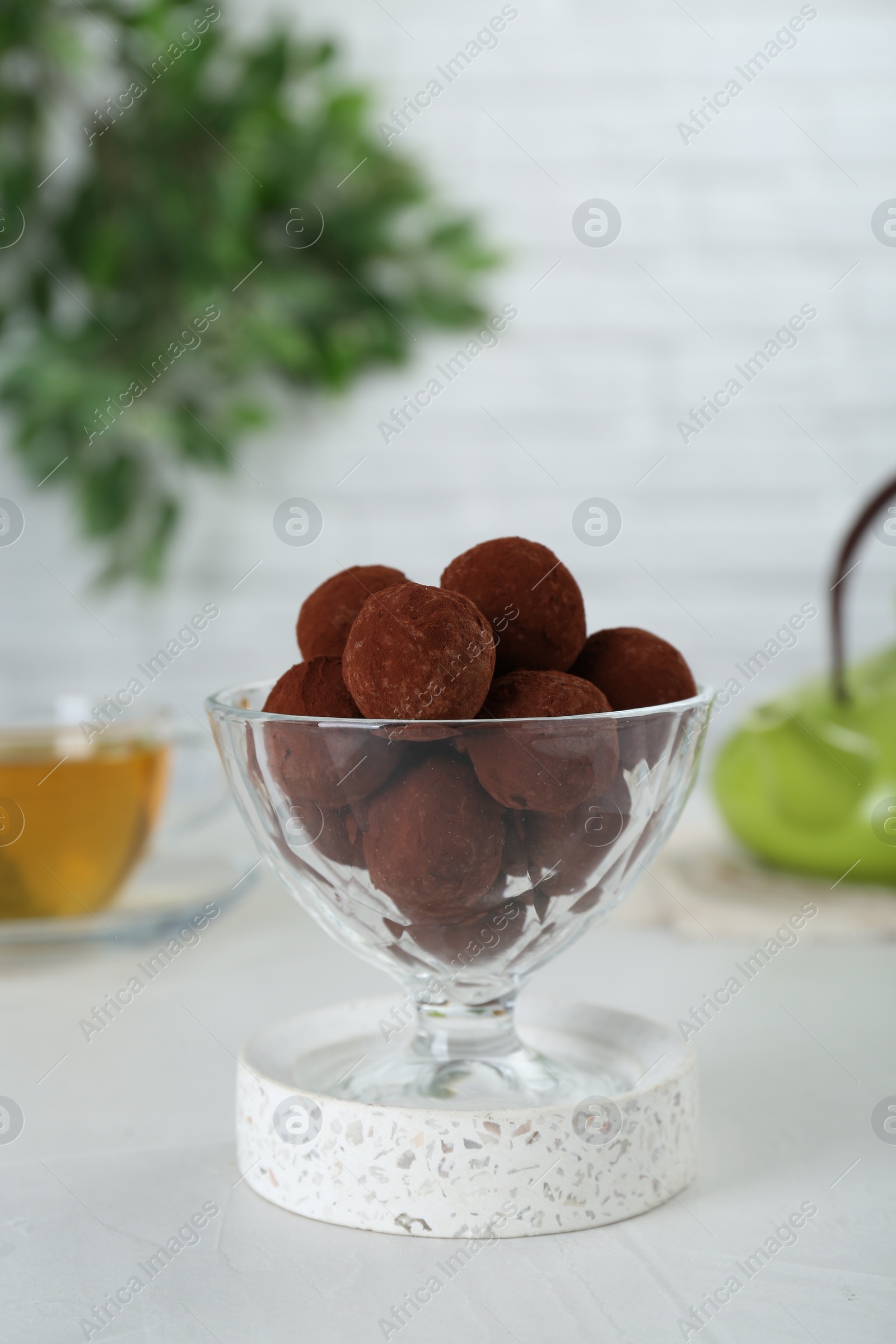 Photo of Dessert glass of delicious chocolate candies powdered with cocoa on white table, closeup