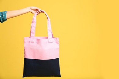 Young woman holding textile bag on yellow background, closeup. Space for text