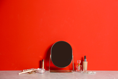 Photo of Small mirror and makeup products on grey marble table near red wall. Space for text