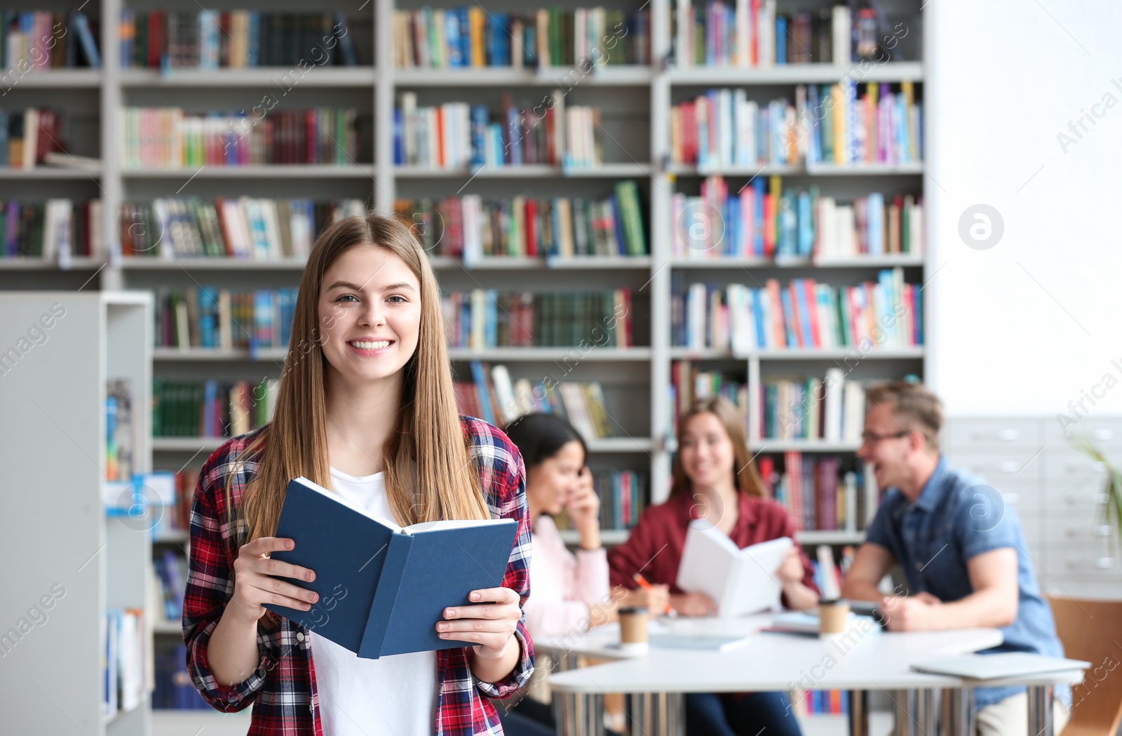 Photo of Young pretty woman with book in library. Space for text