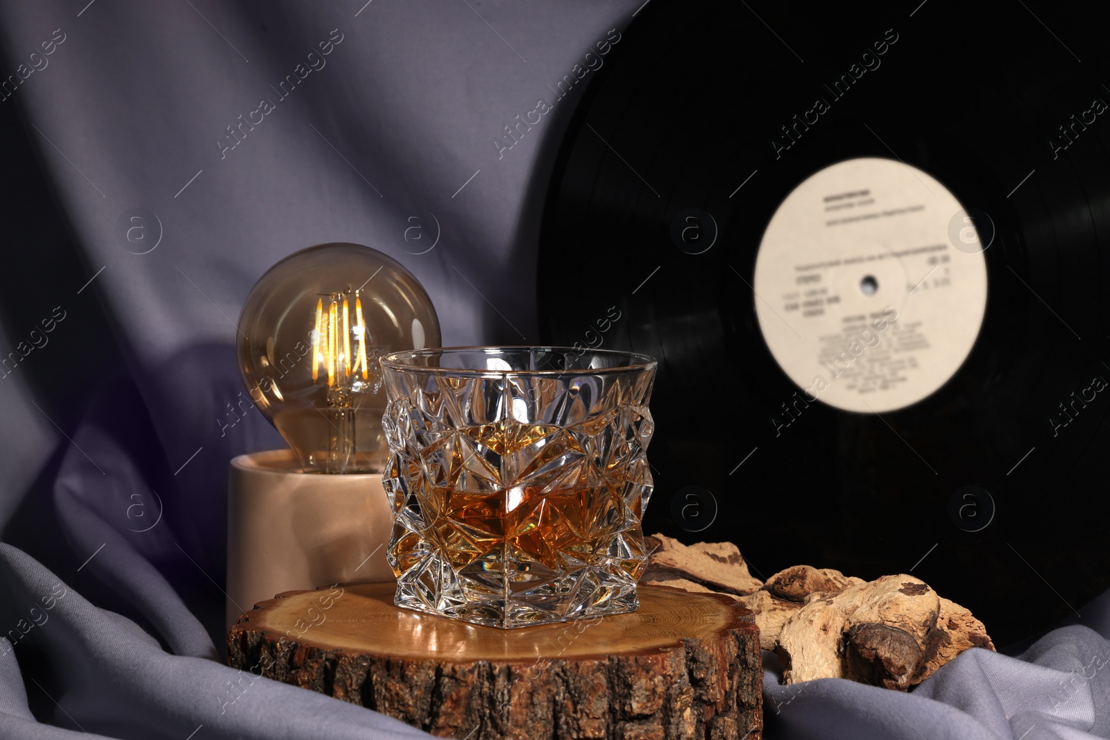 Photo of Glass of tasty alcohol drink, vinyl record and lamp on grey fabric