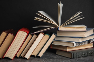 Photo of Stack of hardcover books on grey stone table against black background