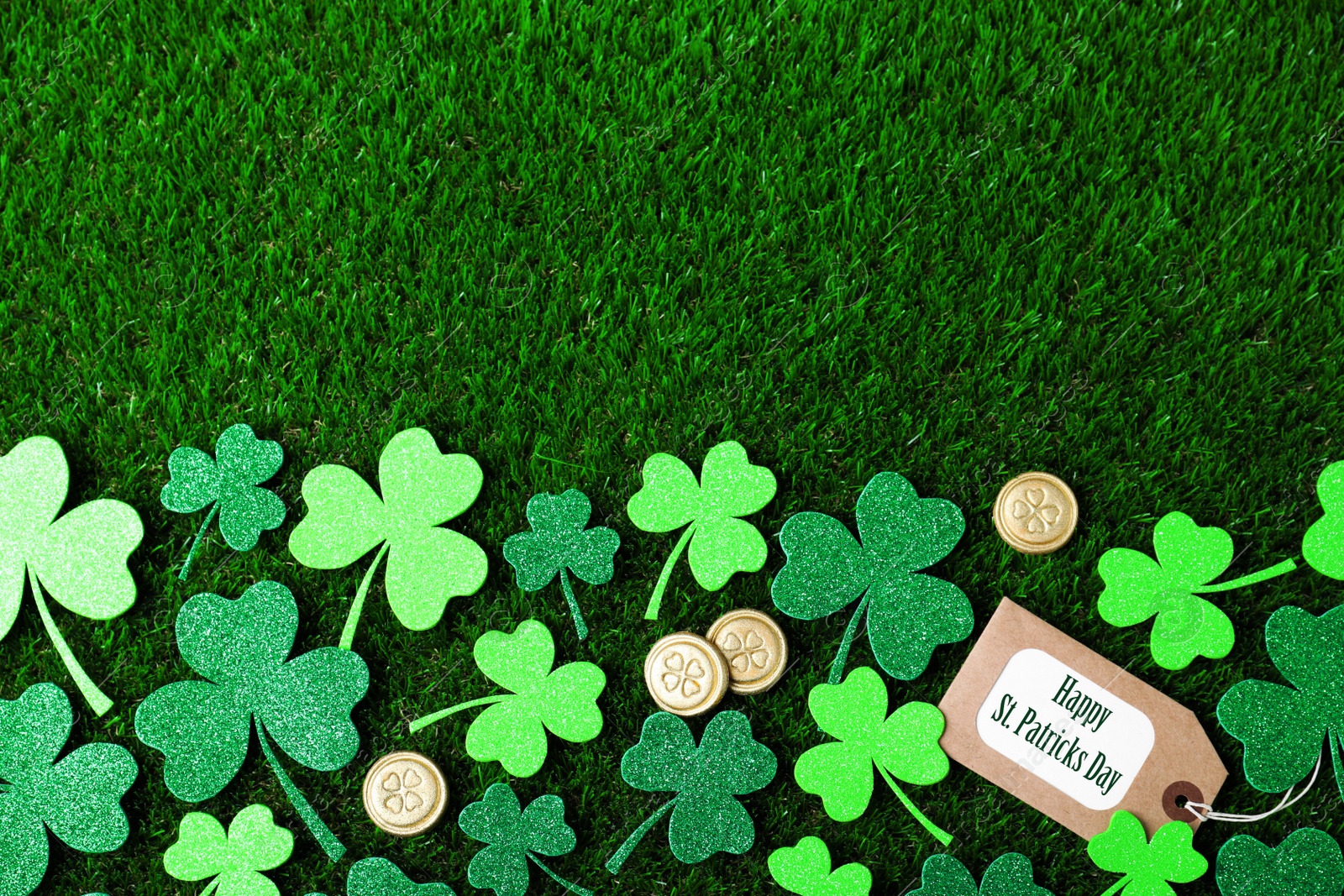 Photo of Flat lay composition with clover leaves and gold coins on green grass, space for text. St. Patrick's Day celebration